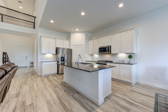 kitchen featuring light wood-type flooring, stainless steel appliances, an island with sink, and white cabinetry