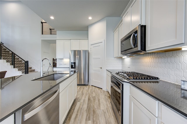 kitchen with white cabinets, backsplash, appliances with stainless steel finishes, light hardwood / wood-style floors, and sink