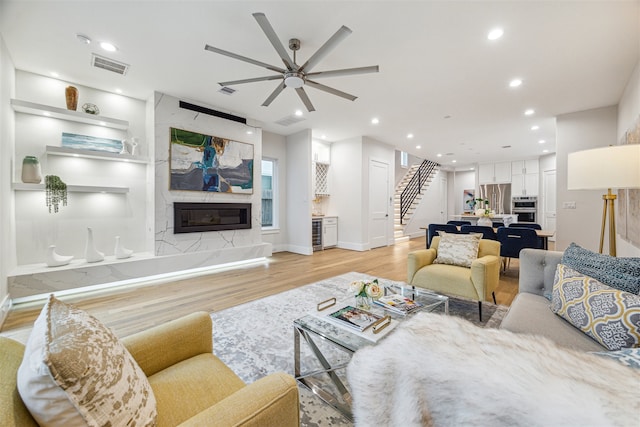 living room featuring a premium fireplace, ceiling fan, and light hardwood / wood-style floors