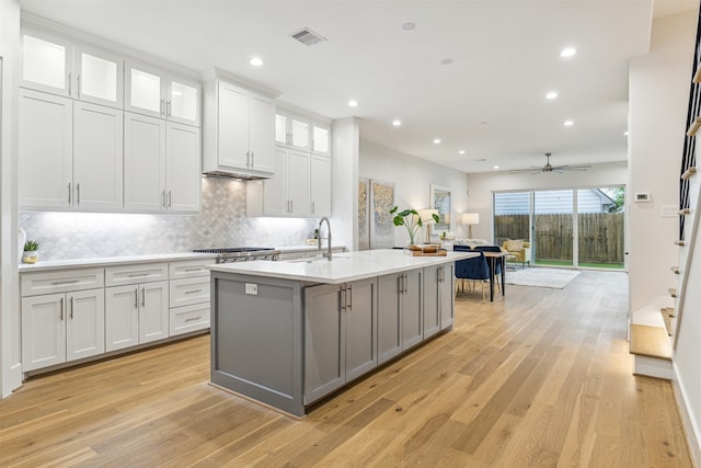 kitchen with a center island with sink, sink, ceiling fan, light hardwood / wood-style floors, and white cabinetry