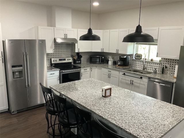 kitchen with a center island, sink, appliances with stainless steel finishes, decorative light fixtures, and white cabinetry