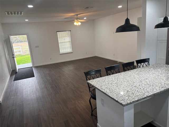 kitchen featuring a breakfast bar, hanging light fixtures, ceiling fan, light stone counters, and dark hardwood / wood-style flooring