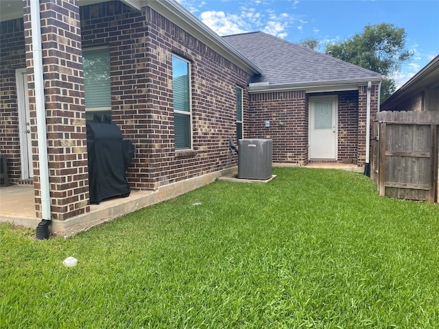 rear view of house featuring fence, roof with shingles, a yard, central AC, and brick siding