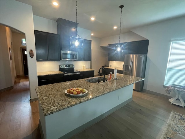 kitchen featuring a kitchen island with sink, a sink, stone countertops, appliances with stainless steel finishes, and dark wood-style flooring