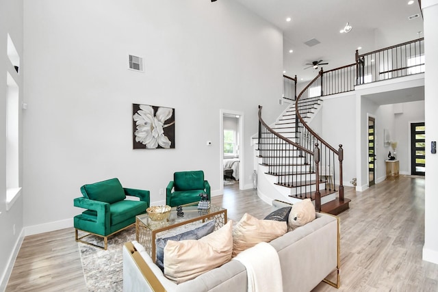 living room featuring light wood-type flooring, ceiling fan, and a high ceiling