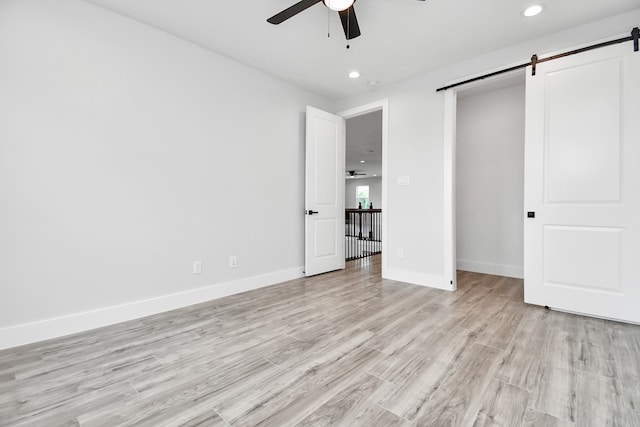 unfurnished bedroom featuring light wood-type flooring, ceiling fan, and a barn door