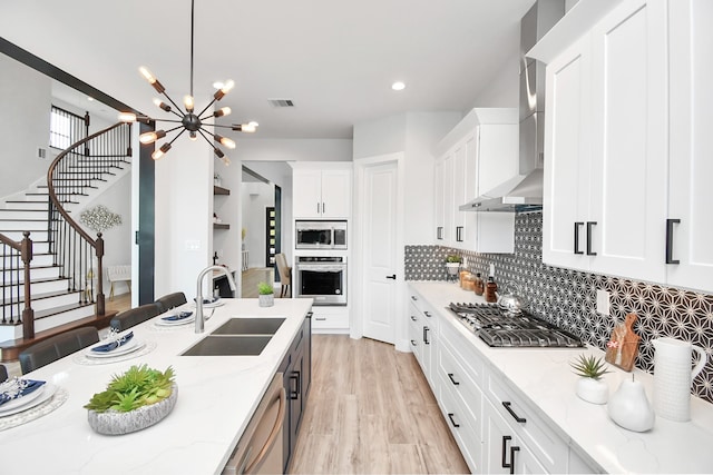 kitchen with light stone countertops, sink, wall chimney range hood, and stainless steel appliances