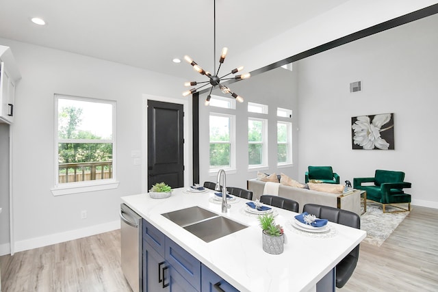 kitchen featuring stainless steel dishwasher, pendant lighting, sink, a center island with sink, and light hardwood / wood-style floors