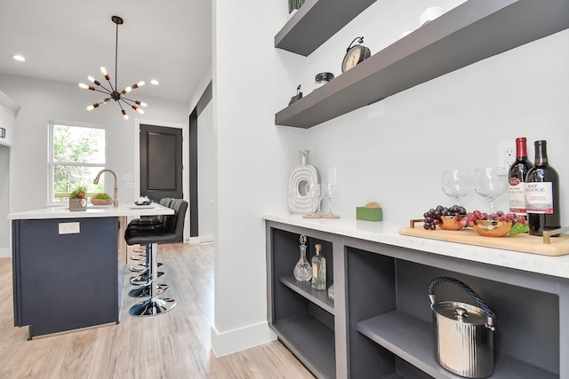 kitchen with light hardwood / wood-style flooring, decorative light fixtures, sink, a kitchen bar, and a notable chandelier