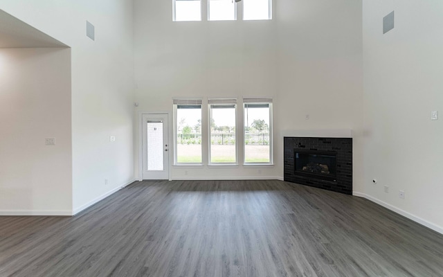 unfurnished living room with a brick fireplace, a towering ceiling, and dark hardwood / wood-style flooring