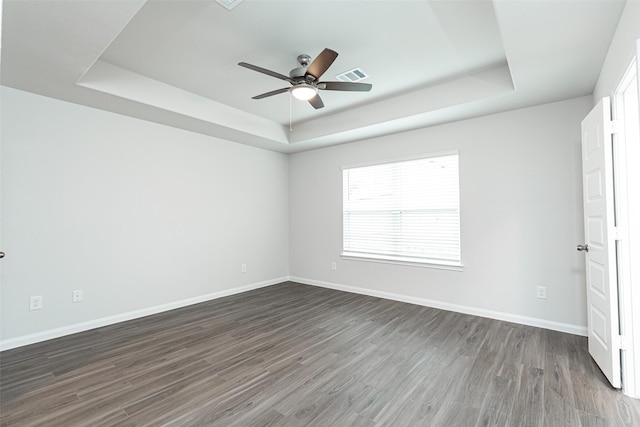 spare room with ceiling fan, a raised ceiling, and dark wood-type flooring