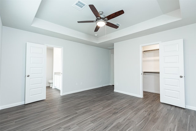 unfurnished bedroom featuring a tray ceiling, a walk in closet, ceiling fan, and connected bathroom