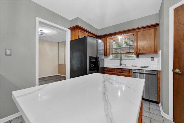 kitchen featuring appliances with stainless steel finishes, backsplash, light stone countertops, light tile patterned floors, and sink