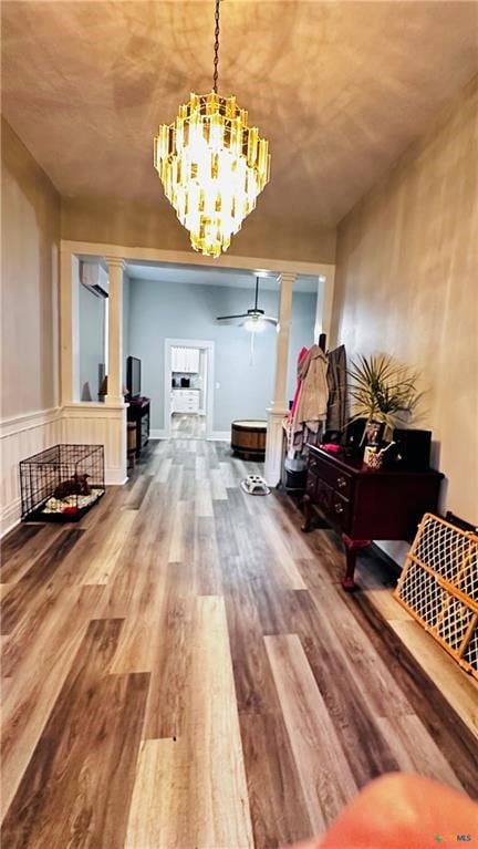 interior space with hardwood / wood-style floors, ceiling fan with notable chandelier, a wall unit AC, and decorative columns