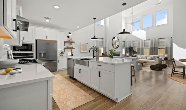 kitchen featuring white cabinetry, sink, an island with sink, decorative light fixtures, and appliances with stainless steel finishes