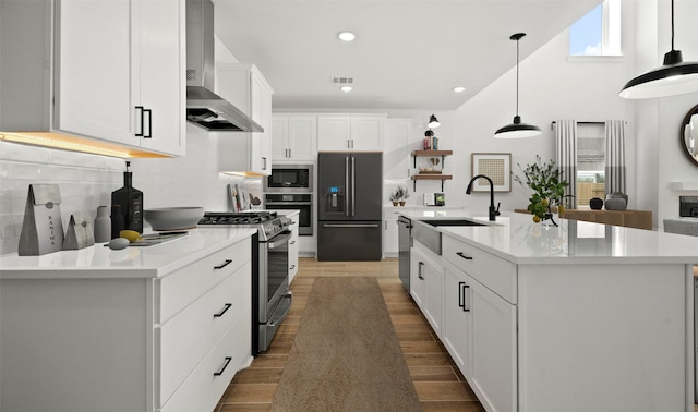 kitchen with appliances with stainless steel finishes, a kitchen island with sink, and wall chimney range hood