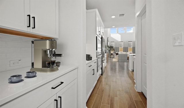 bar featuring white cabinetry, stainless steel microwave, and wood-type flooring