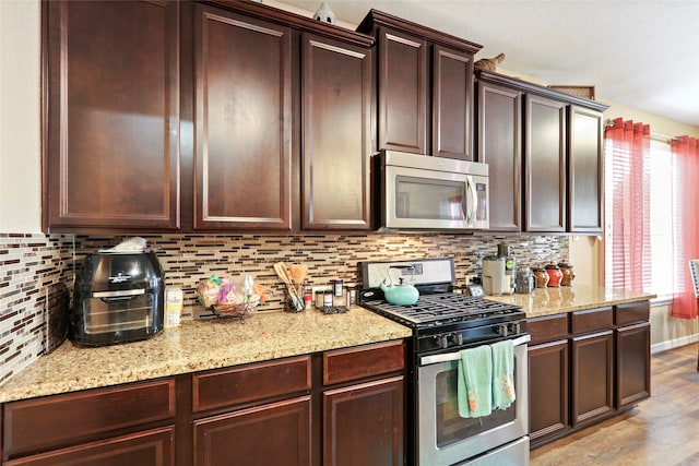 kitchen featuring light stone counters, backsplash, stainless steel appliances, and light wood-type flooring