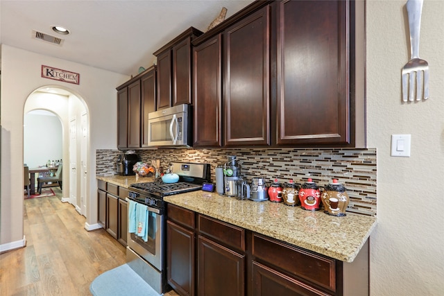 kitchen with decorative backsplash, light hardwood / wood-style floors, light stone countertops, pendant lighting, and stainless steel appliances