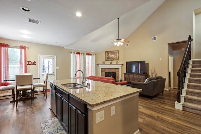 kitchen with ceiling fan, sink, a center island with sink, a tiled fireplace, and dark wood-type flooring