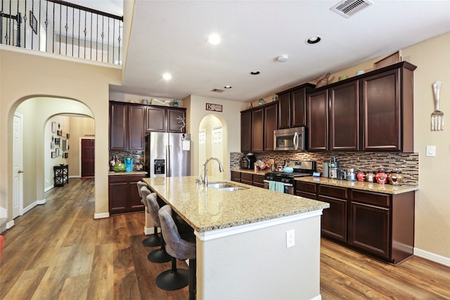 kitchen with an island with sink, sink, tasteful backsplash, appliances with stainless steel finishes, and hardwood / wood-style floors