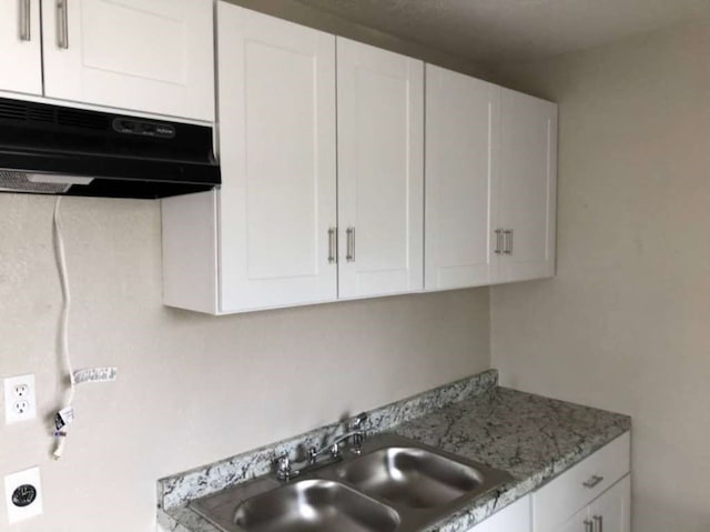 kitchen featuring white cabinetry, light stone counters, and sink