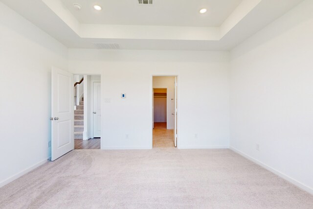 unfurnished bedroom with a tray ceiling, a spacious closet, and light carpet