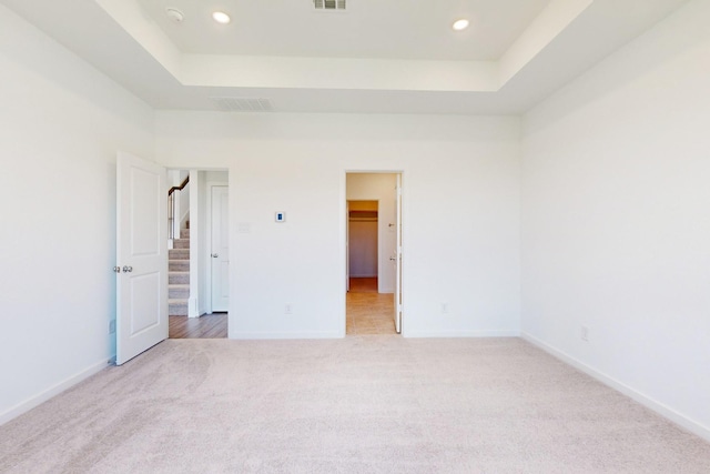 unfurnished bedroom with light carpet, baseboards, visible vents, and a raised ceiling