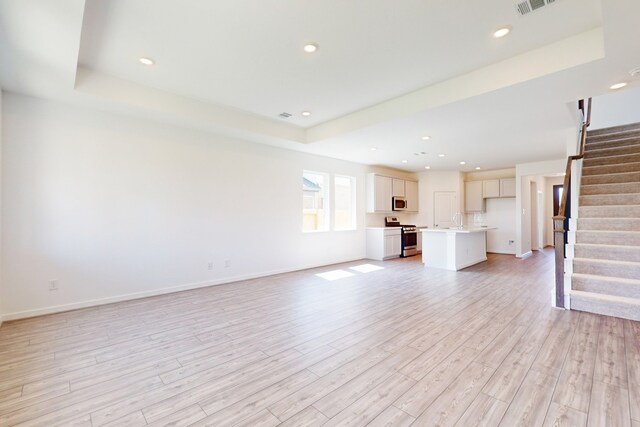 unfurnished living room featuring sink, a tray ceiling, and light hardwood / wood-style floors