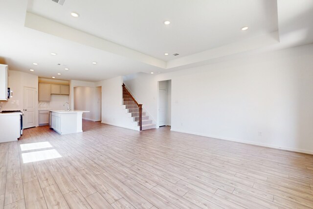 unfurnished living room with a tray ceiling, light hardwood / wood-style flooring, and sink