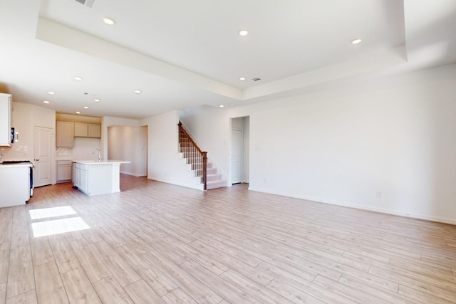 unfurnished living room featuring stairs, a tray ceiling, and light wood finished floors