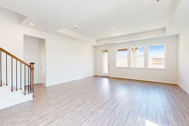 empty room with a raised ceiling and light hardwood / wood-style flooring