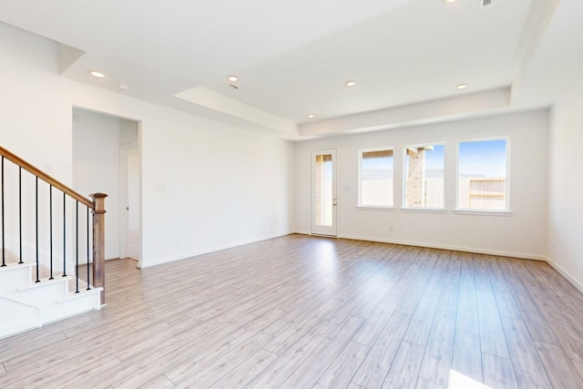 unfurnished living room with light wood finished floors, stairs, a raised ceiling, and recessed lighting