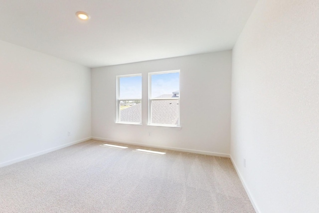 spare room featuring light carpet and baseboards