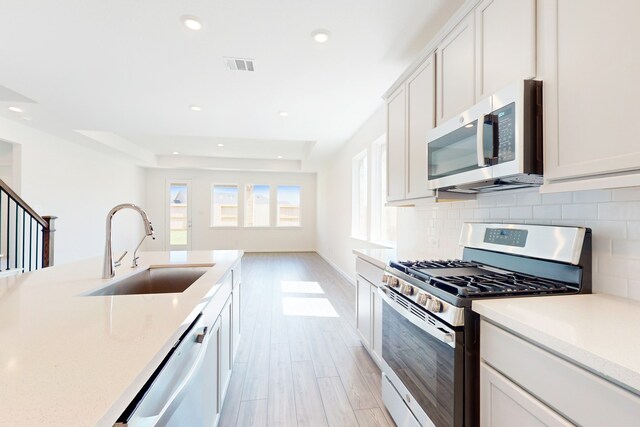 kitchen featuring light wood-type flooring, sink, a tray ceiling, appliances with stainless steel finishes, and white cabinets