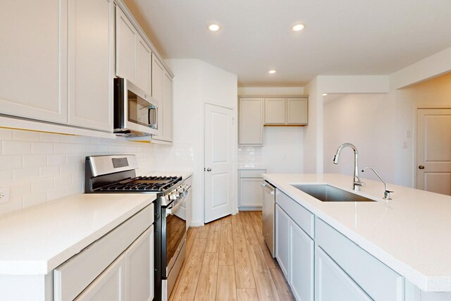 kitchen featuring backsplash, light hardwood / wood-style flooring, appliances with stainless steel finishes, sink, and an island with sink