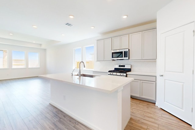 kitchen featuring stainless steel appliances, a sink, visible vents, light wood-style floors, and an island with sink