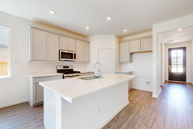 kitchen with light wood-type flooring, sink, appliances with stainless steel finishes, and a kitchen island with sink