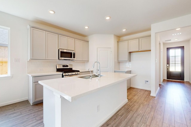 kitchen with decorative backsplash, an island with sink, appliances with stainless steel finishes, light wood-style floors, and a sink