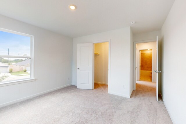 unfurnished bedroom featuring a closet, light colored carpet, and a spacious closet