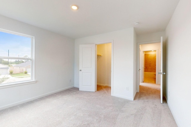 unfurnished bedroom featuring light carpet, a spacious closet, and baseboards