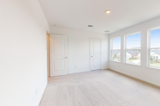 empty room featuring light colored carpet, visible vents, and baseboards