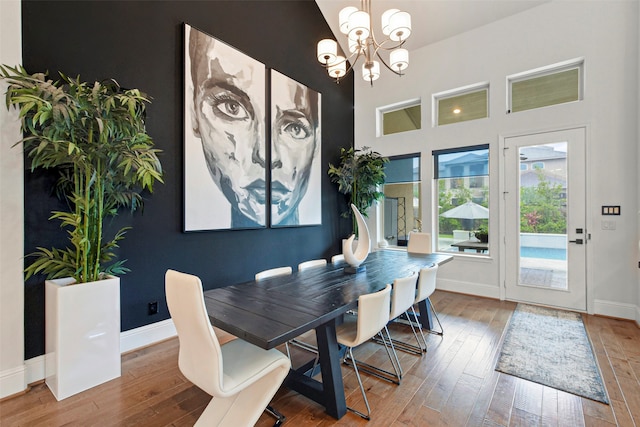 dining room with wood-type flooring, a towering ceiling, and a notable chandelier