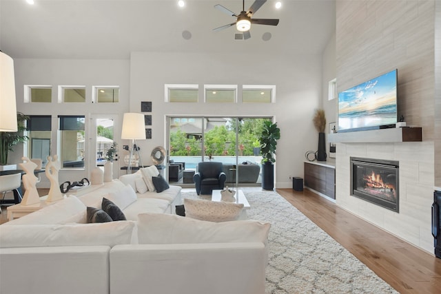 living room with light wood-type flooring, a tiled fireplace, ceiling fan, and high vaulted ceiling