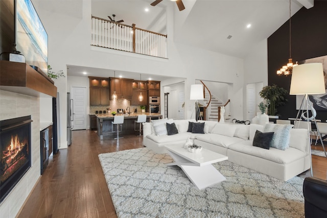 living room with high vaulted ceiling, beam ceiling, a tiled fireplace, and dark wood-type flooring