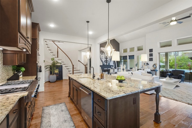 kitchen featuring pendant lighting, hardwood / wood-style floors, light stone counters, and a kitchen island with sink