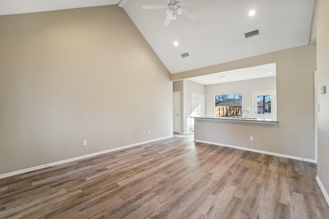 unfurnished living room featuring hardwood / wood-style floors, high vaulted ceiling, sink, ceiling fan, and beam ceiling