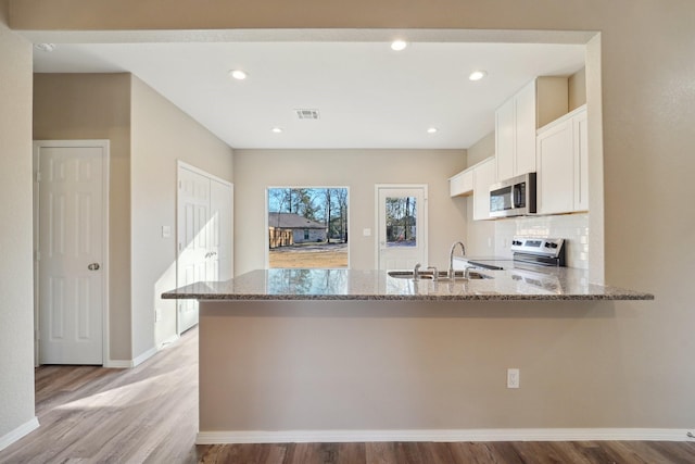 kitchen with light stone countertops, kitchen peninsula, white cabinets, and appliances with stainless steel finishes