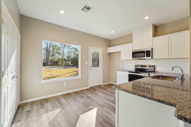 kitchen with sink, white cabinetry, light hardwood / wood-style flooring, dark stone countertops, and stainless steel appliances