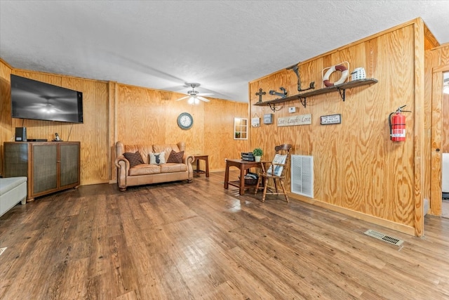 living room with wood-type flooring, a textured ceiling, wood walls, and ceiling fan